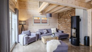 A modern living room with a sofa set, a coffee table, a fireplace, and a large window. - Bergwaldlodge Einklang (Wernigerode)