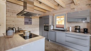 A modern kitchen with wooden beams, stainless steel appliances, and a large window. - Bergwaldlodge Einklang (Wernigerode)