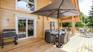 A wooden deck with outdoor furniture, a grill, and a pergola with an umbrella. - Bergwaldlodge Einklang (Wernigerode)
