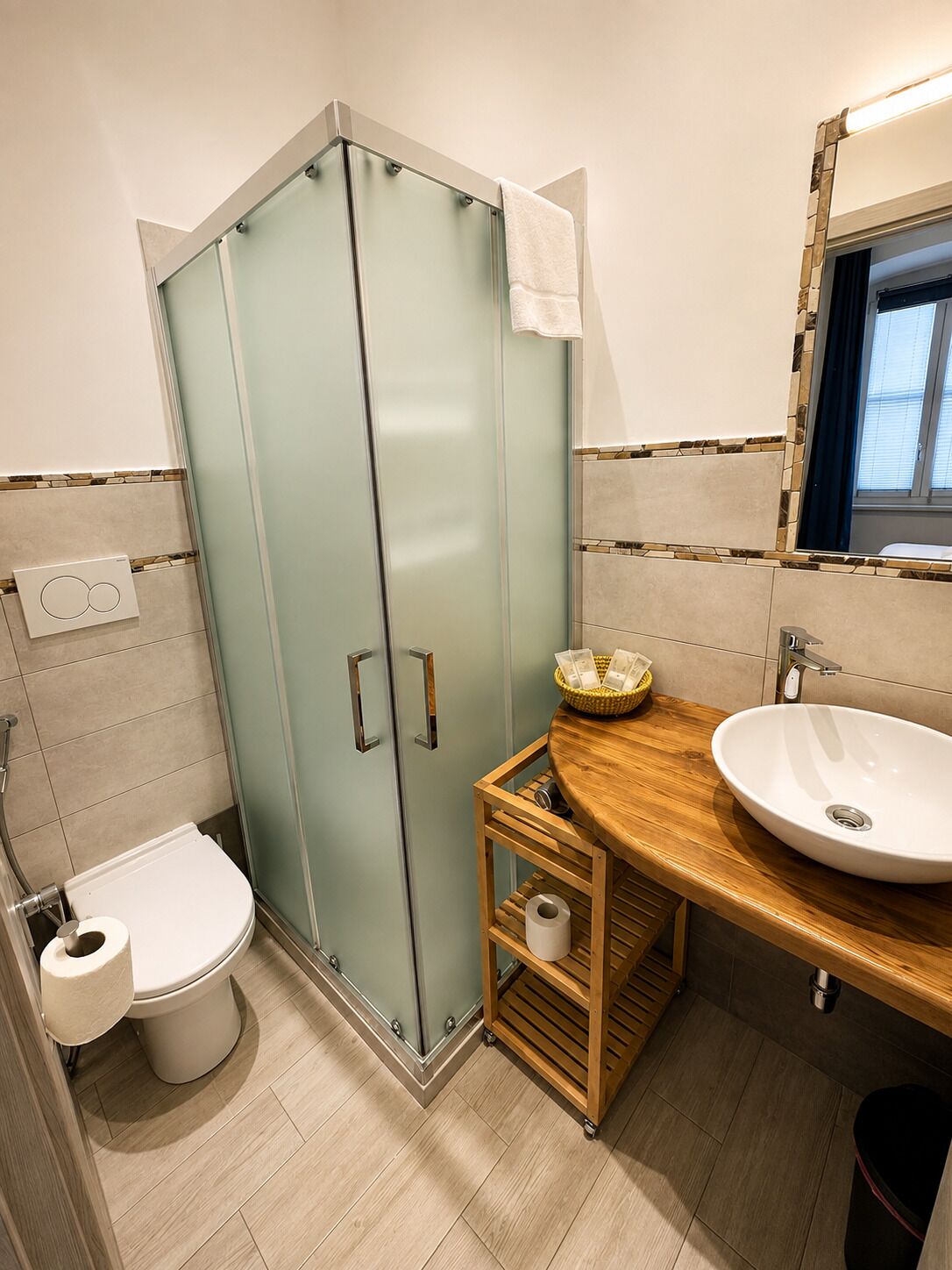 Un baño con cabina de ducha de vidrio, inodoro, lavamanos con encimera de madera y espejo sobre el lavamanos.