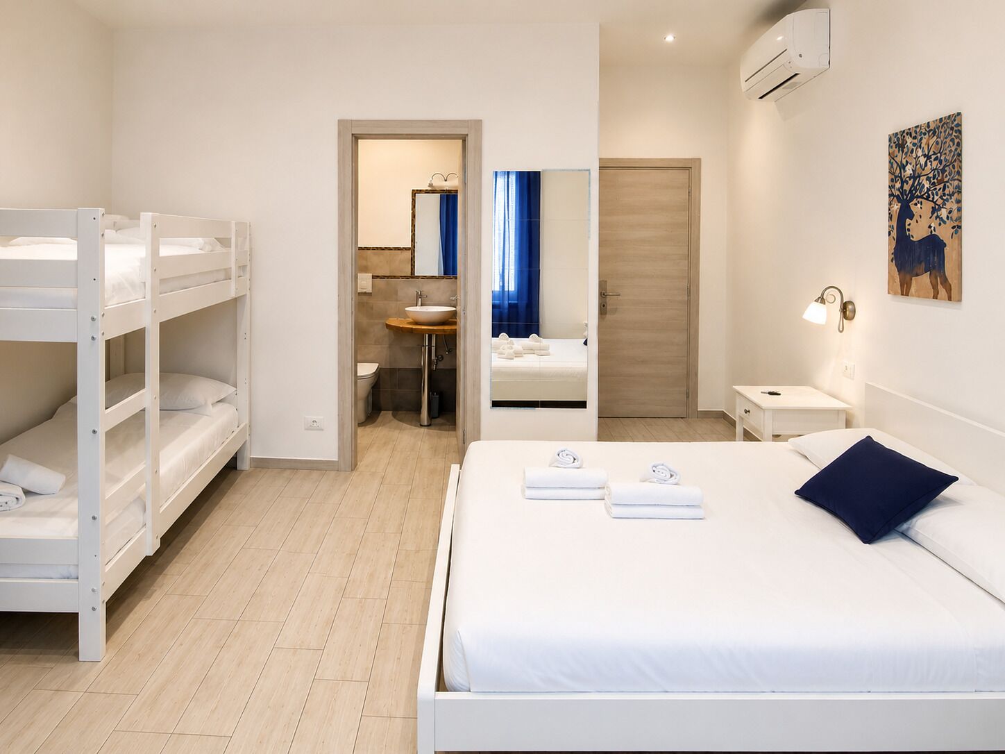 Ein Hotelzimmer mit Etagenbetten, einem Einzelbett, einem Badezimmer mit Spiegel und einem Nachttisch.