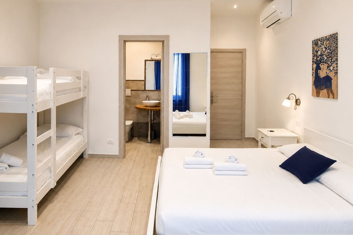 Et hotelværelse med køjesenge, en enkeltseng, et badeværelse med et spejl og et natbord.