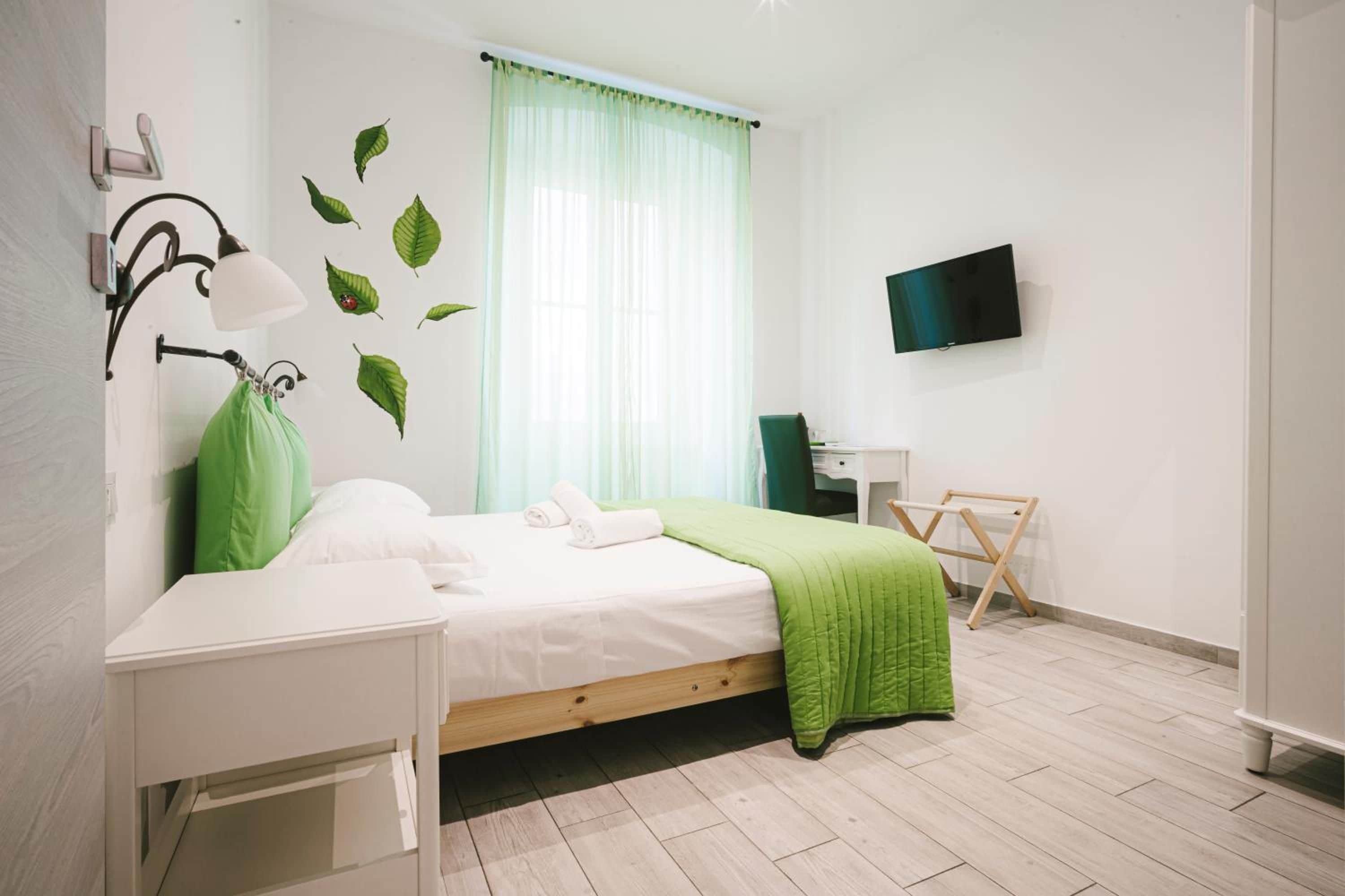 Un dormitorio con cama, escritorio, silla, televisor y ventana con cortinas.