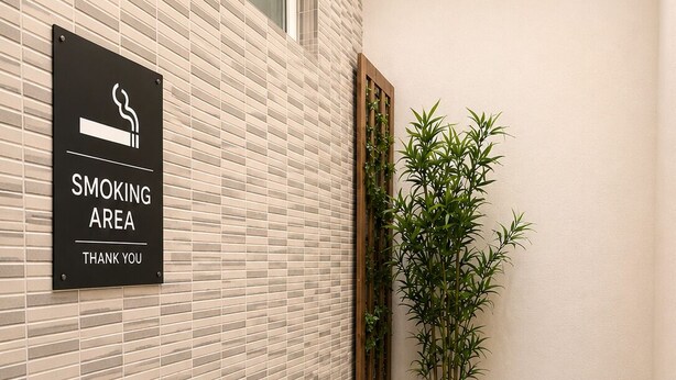 A smoking area with a sign, a wooden table, two potted plants, and a tiled floor. - ROSSETTI ROOMS (Trieste)