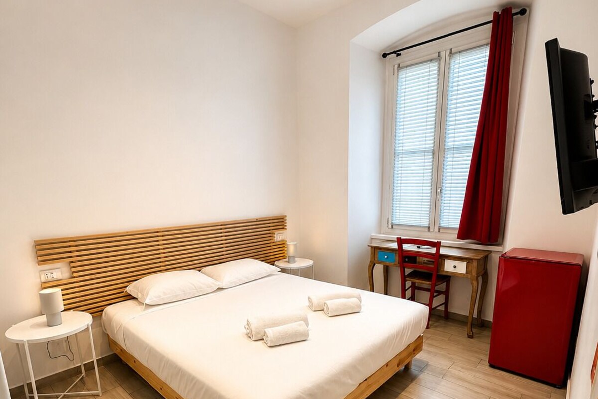 Et hotelværelse med seng, natbord, lampe, stol, skrivebord og fjernsyn.