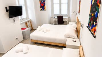 A hotel room with two wooden beds, a desk, a chair, a TV, and artwork on the walls.