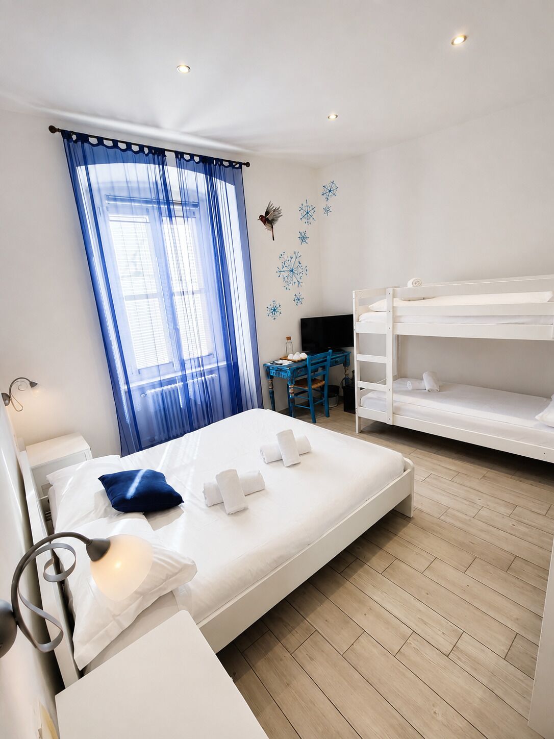 Una habitación de hotel con cama, escritorio, literas y ventana con cortinas.
