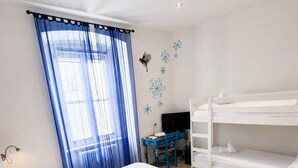 Una habitación de hotel con cama, escritorio, literas y ventana con cortinas.