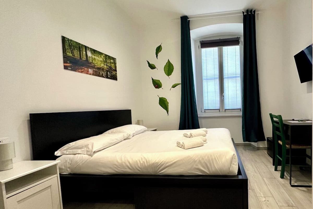 Moderni hotellihuone, jossa on sänky, työpöytä, tuoli, televisio ja ikkuna, jossa on verhot.