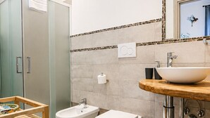 A modern bathroom with a shower enclosure, bidet, sink, and a wooden vanity. - ROSSETTI ROOMS (Trieste)