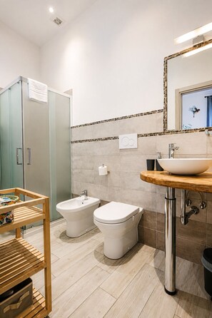 Et stilfuldt badeværelse med bruseniche, bidet, vask og et træskab.