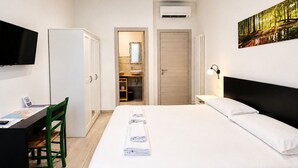 A hotel room with a bed, a desk with a chair, a television, and a painting on the wall. - ROSSETTI ROOMS (Trieste)