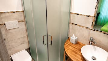A bathroom with a glass-enclosed shower, a toilet, a sink with a wooden vanity, and a mirror.