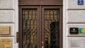 A double door with a geometric glass pattern, a plaque with a name, and a number sign indicating the building's address. - ROSSETTI ROOMS (Trieste)