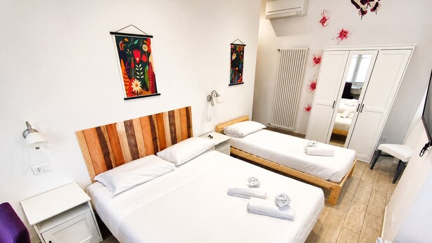 Habitación de hotel con dos camas, un armario, un espejo y obras de arte en las paredes.
