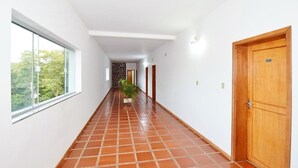 Un pasillo con suelo de baldosas, una puerta de madera a la derecha y una ventana a la izquierda.