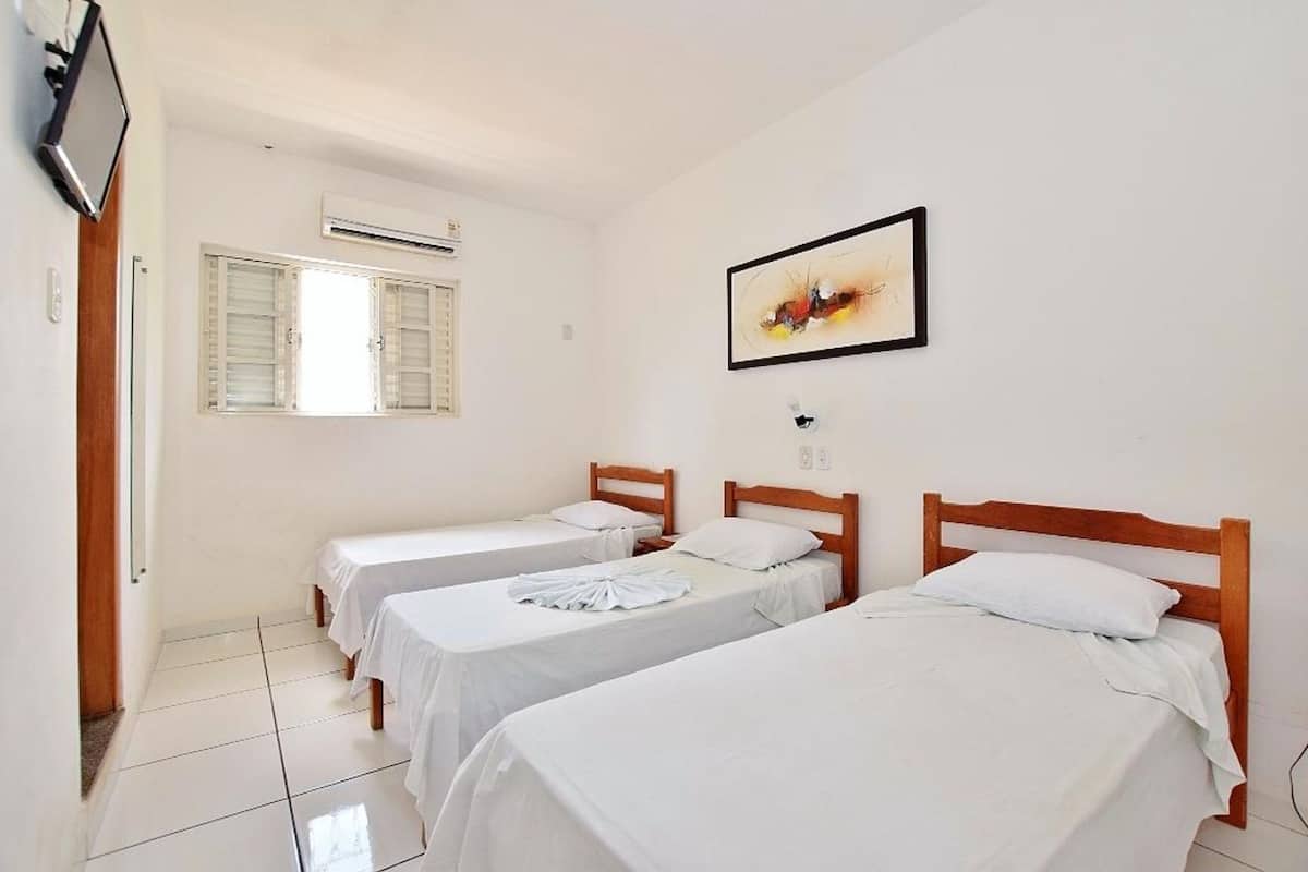 Quarto de hotel com duas camas de solteiro, janela com persianas, ar condicionado e um quadro abstrato na parede.