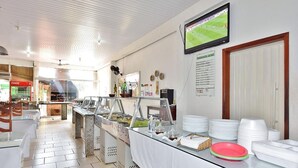 Zona de bufé con varias estaciones de comida, un televisor montado en la pared y un tablero de menú.