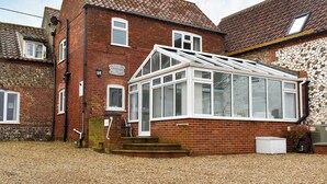 A two-story brick house with a conservatory, a stone wall, and a gravel driveway. - 3 bedroom accommodation in Brancaster Staithe, near Wells-next-the-Sea (Brancaster Staithe, near Wells-next-the-Sea)