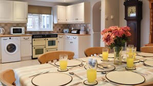 A modern kitchen with white cabinetry, a built-in oven, a microwave, and a coffee machine. There is a dining table set with plates, cutlery, and glasses of orange juice. - 3 bedroom accommodation in Brancaster Staithe, near Wells-next-the-Sea (Brancaster Staithe, near Wells-next-the-Sea)