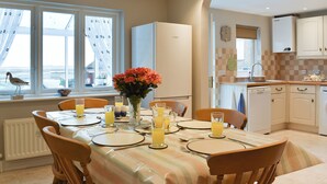 A modern kitchen with white cabinets, a Bosch refrigerator, and a dining area set for breakfast with orange juice and a vase of flowers. - 3 bedroom accommodation in Brancaster Staithe, near Wells-next-the-Sea (Brancaster Staithe, near Wells-next-the-Sea)