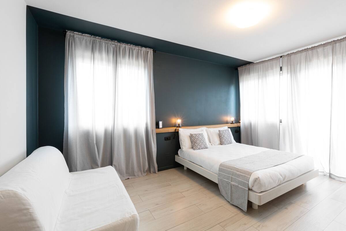 A modern hotel room with a bed, a sofa, and a nightstand.