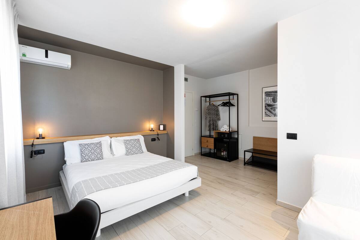 A modern hotel room with a large bed, bedside tables, a desk, and a wardrobe.