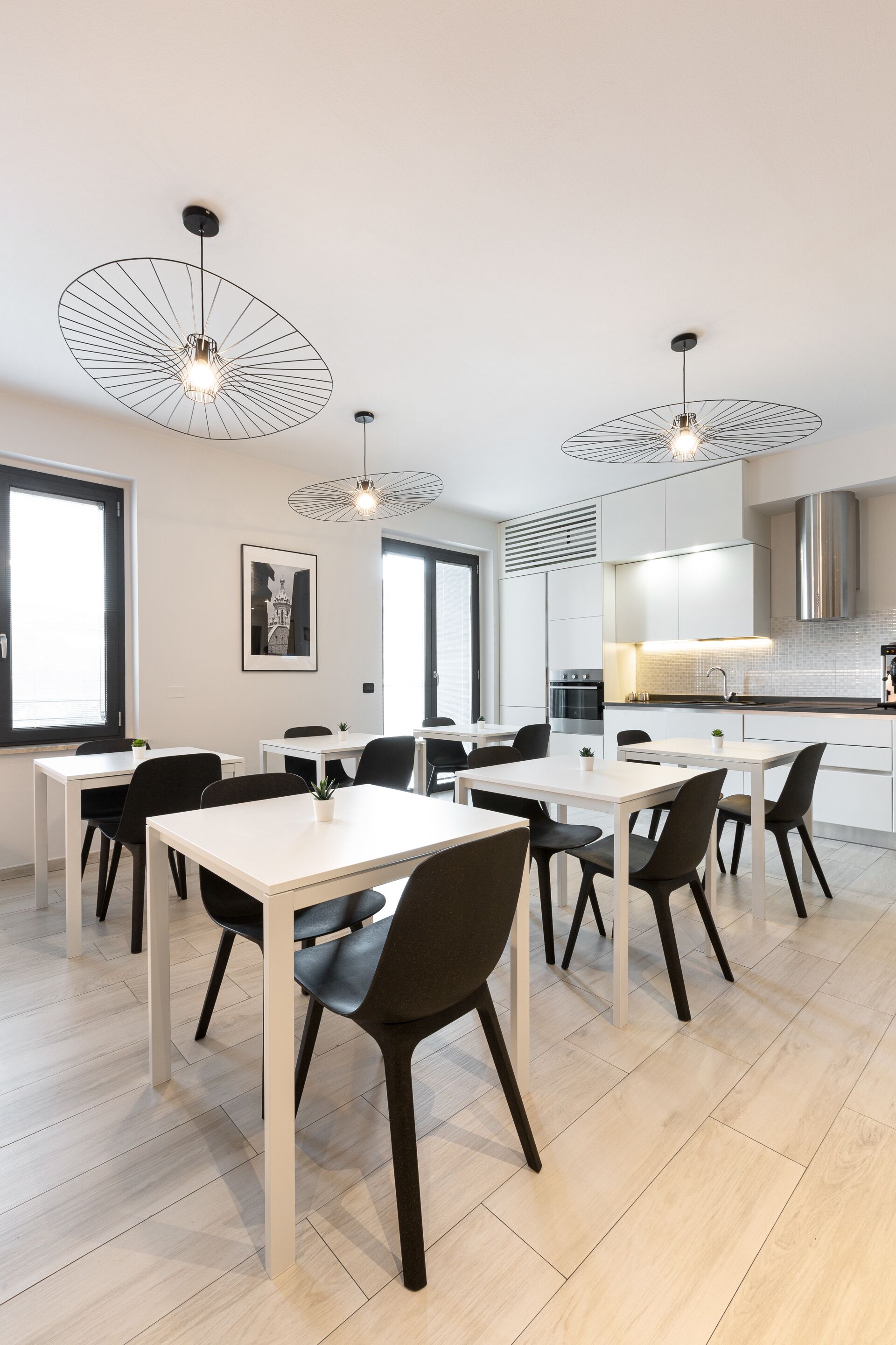 Una cocina moderna con armarios blancos, una campana extractora de acero inoxidable y horno integrado. Hay dos lámparas colgantes con un diseño de alambre original.