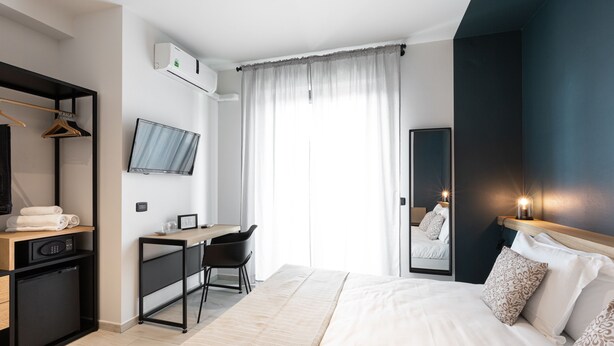 Et moderne hotelværelse med seng, skrivebord, stol og et tv ophængt på væggen.