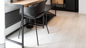 Et moderne hotelværelse med skrivebord i træ, fladskærms-tv, et garderobeskab med hængende tøj og et lille tekøkken.