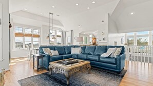 A spacious living room with a blue sectional sofa, a wooden coffee table, and a large window providing a view of the outdoors.