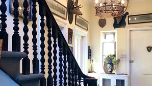 A grand staircase with ornate balusters, a chandelier, and a door with a shield decoration.