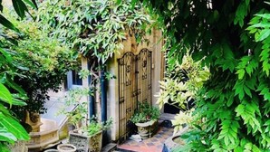 A stone-paved courtyard with a wrought iron gate, surrounded by lush greenery and potted plants.