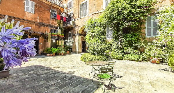 A courtyard with a table and chairs, potted plants, and a building with balconies.