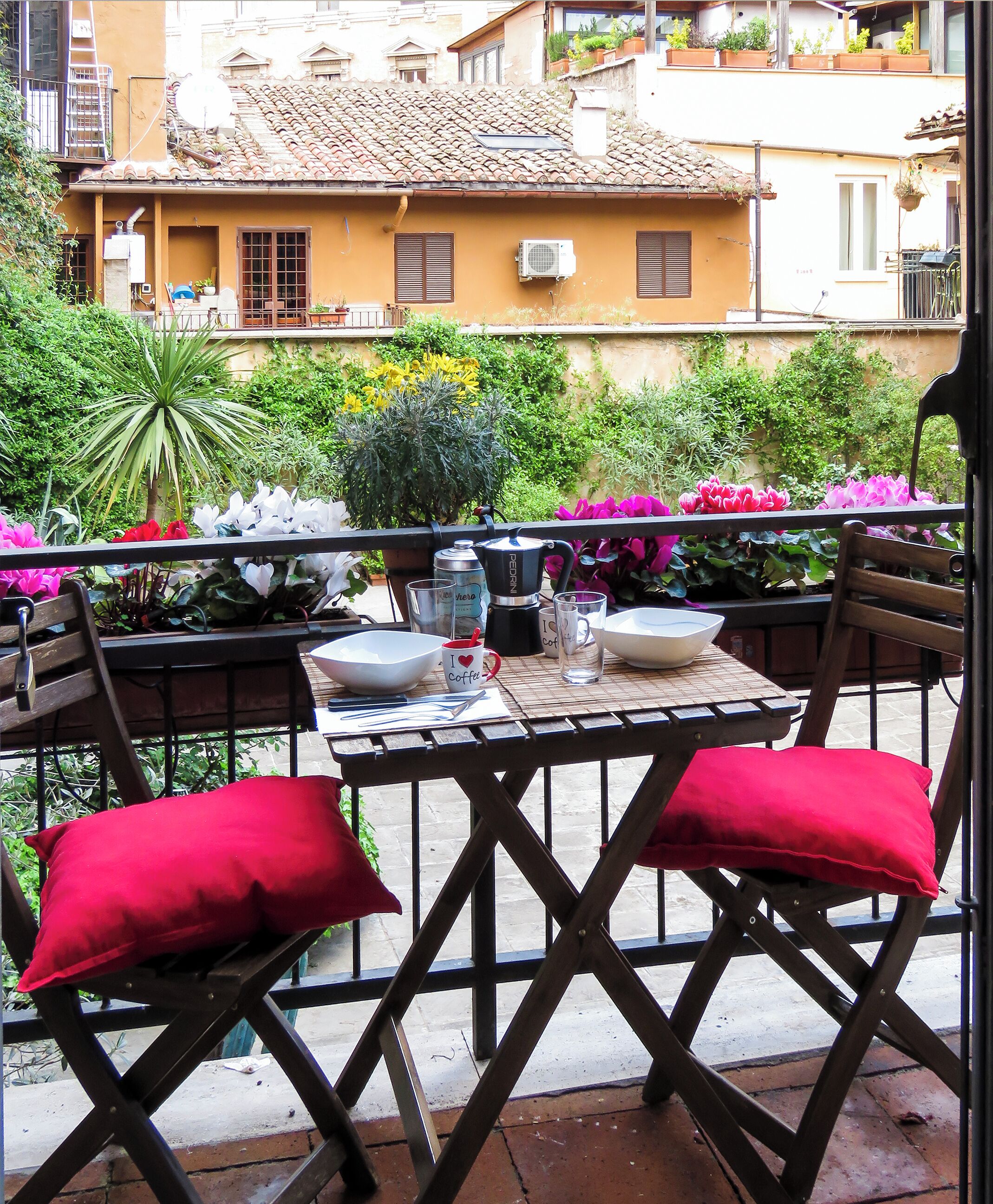 Un balcon avec une table dressée pour deux personnes, agrémentée d’une cafetière, de tasses et d’un bol.