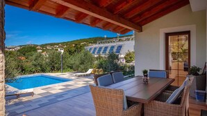 Uma área externa coberta com piscina, móveis de vime e vista para um edifício com painéis solares.