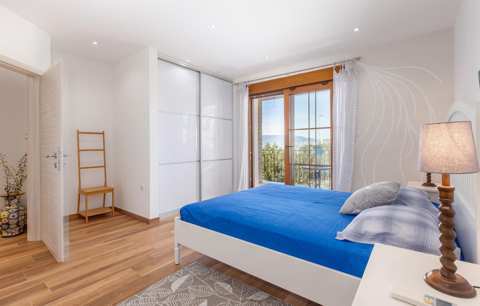 Ein Schlafzimmer mit Bett, Nachttisch, Lampe, Fenster mit Aussicht und Holzboden.