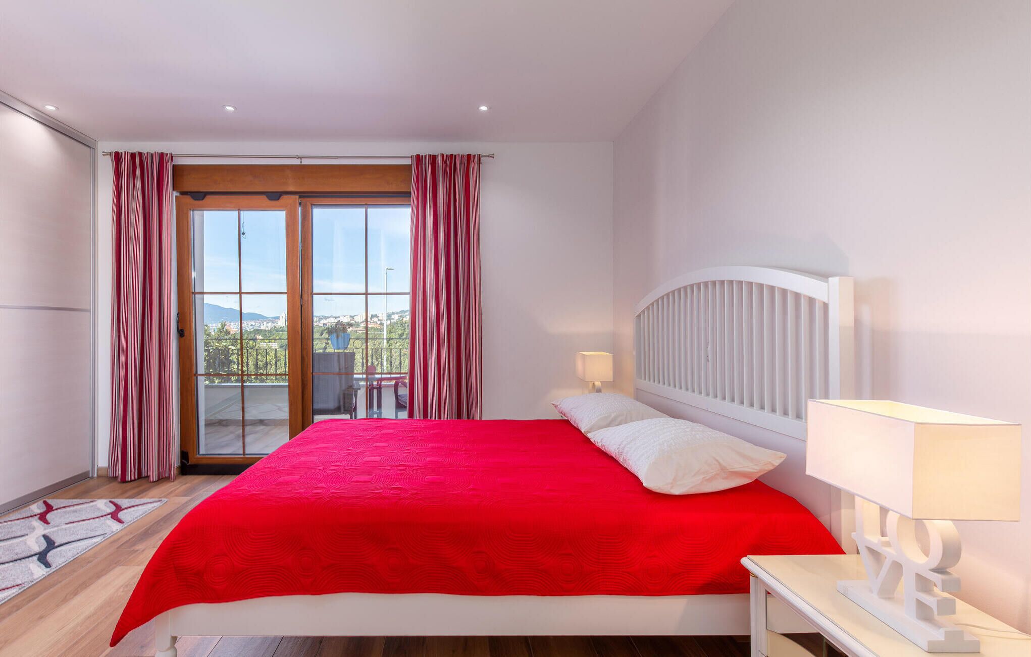 A bedroom with a large bed, a nightstand, a lamp, and a view through a glass door to an outdoor balcony.