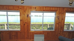 Habitación con paredes de madera, ventana con vista a un lago, un calentador y una silla.