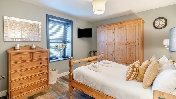 Ein Schlafzimmer mit einem hölzernen Bett, einem Schminktisch und einem Fernseher an der Wand.