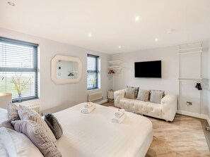 Un dormitorio moderno con una cama grande, un sofá blanco, un televisor y estanterías empotradas.