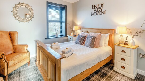 A bedroom with a bed, a chair, a nightstand, a lamp, a mirror, and a window. - 5 bedroom accommodation in Bowness-on-Solway (Bowness-on-Solway)