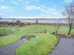 A grassy area with a circular stone feature, a gravel path, and a view of a body of water.