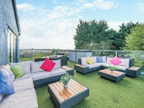Un patio exterior con mobiliario de mimbre, una mesa de centro de madera y vistas al campo.