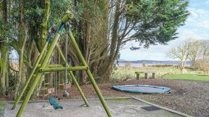 A playground with a swing set, a trampoline, and a bench. - 5 bedroom accommodation in Bowness-on-Solway (Bowness-on-Solway)