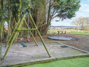 Une aire de jeux avec des balançoires, un trampoline et un banc.