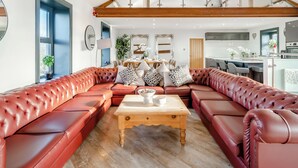 A modern living room with a sectional sofa, a wooden coffee table, and a dining area with a large mirror and chandelier. - 5 bedroom accommodation in Bowness-on-Solway (Bowness-on-Solway)