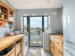 Eine Küche mit Waschmaschine, Holzschränken, einem Spülbecken und einem Fenster mit Blick auf einen Garten.