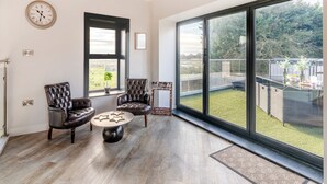 Ein geräumiges Wohnzimmer mit großem Fenster, einem runden Couchtisch, zwei Ledersesseln und einer Wanduhr.