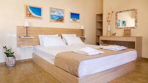 A hotel room with a wooden bed, white linens, a bedside table with a lamp, a potted plant, and artwork on the walls. - Avra Apartments (Apokoronas)
